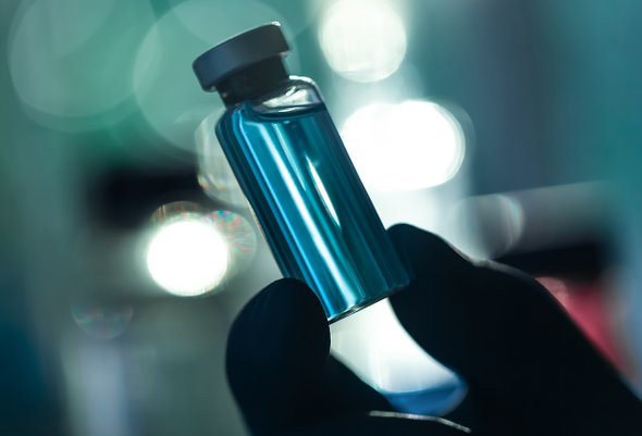 Силуэт руки в перчатке держит флакон с вакциной. Вакцина от рака, лекарство от рака