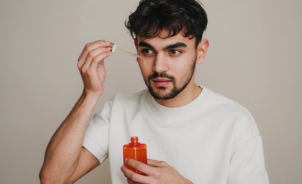 Мужчина наносит косметическую сыворотку на лицо. Мужской уход за кожей лица