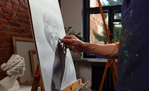 Академический рисунок. Мужчина рисует карандашом голову античной статуи на мольберте