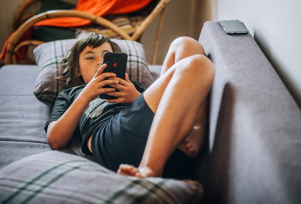 Ленивый ребенок валяется на диване с телефоном / смартфоном. Мотивация у детей