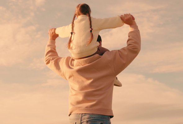 Дочка сидит на плечах отца во время заката