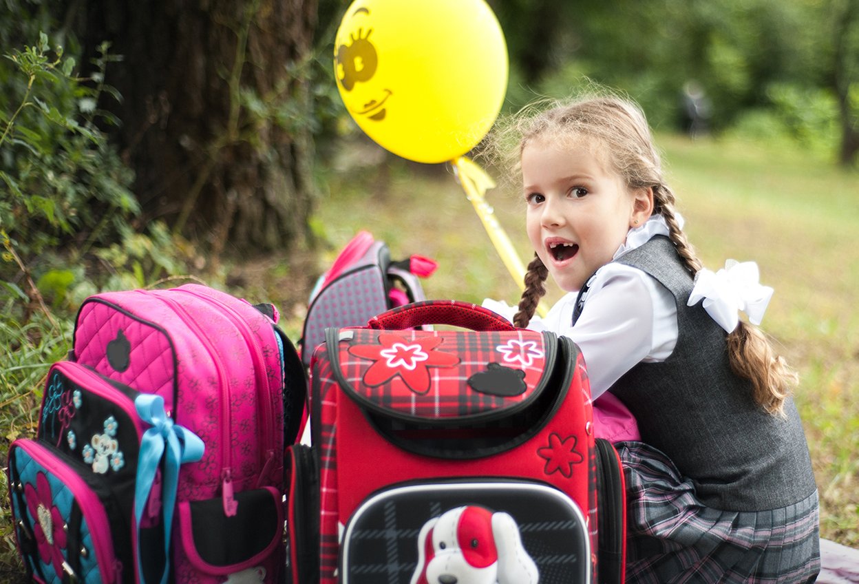 1 сентября. Девочка первоклассница с воздушными шариками и рюкзаками на природе. Вид со спины. Выбор школы