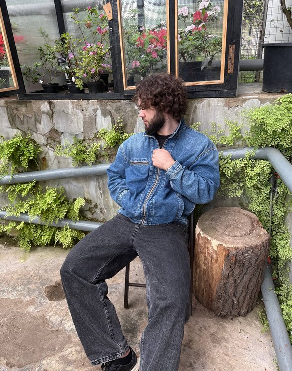 Учитель математики. Мужчина в джинсовой куртке сидит на стуле на фоне стены с цветами