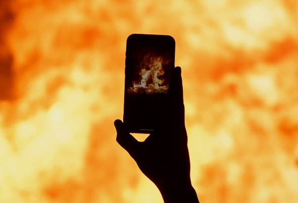 Рука со смартфоном снимает большой костер. Огонь. Родительский чат