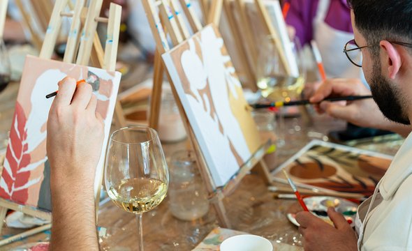 Арт-вечеринка. Взрослые мужчины и женщины рисуют на мольберте красками с вином
