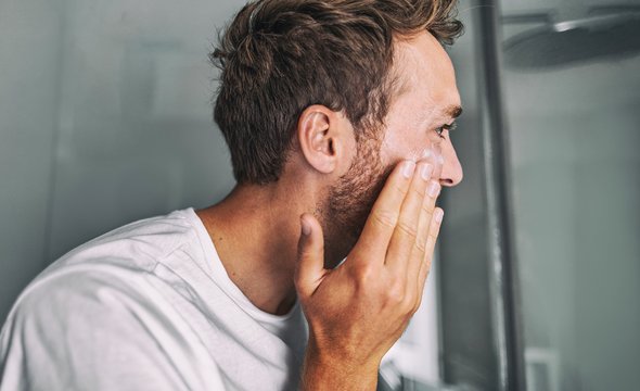 Мужчина наносит крем на кожу лица. Мужской уход за кожей лица