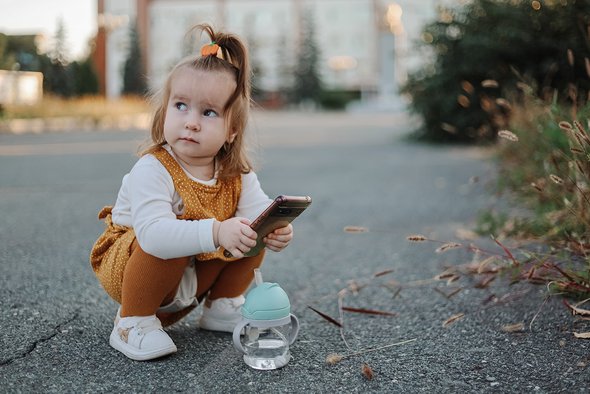 Ребенок тоддер сидит на корточках на улице с телефоном в руках. Кто такие «шелковистые» мамы. Silky mom