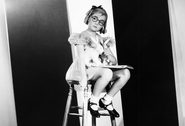 Девочка дошкольница сидит на большом стуле с книгой и игрушками-зайцами. Мягкая подготовка ребенка к школе